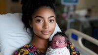 Young African American mother holding newborn baby in hospital room, wearing colorful floral top, expressing tender loving care and maternal bond in healthcare setting.
