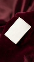 Blank white clothing label on burgundy velvet fabric with soft folds and rich texture for fashion branding and garment manufacturing concepts.