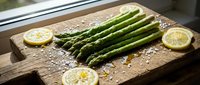Fresh green asparagus spears arranged on rustic wooden cutting board with lemon slices and sea salt crystals for healthy cooking and meal preparation.