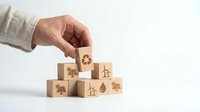 Hand placing wooden cube with recycling symbol on pyramid of eco-friendly blocks featuring renewable energy icons for sustainable business concepts.