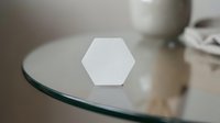 White hexagon shape on glass table surface with soft lighting and blurred background elements creating minimalist geometric composition for modern design projects.