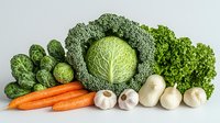 Fresh organic vegetables arranged in row including savoy cabbage, carrots, brussels sprouts, garlic, mushrooms and lettuce on white background. Healthy eating concept.