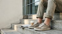 Man sitting on outdoor steps with coffee cup and newspaper, wearing casual khaki pants and sneakers, urban lifestyle concept.