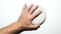 Male hand holding white oval soap bar against clean background for hygiene and skincare product advertising.