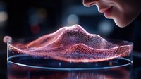 Glowing red particles forming mountain landscape silhouette in petri dish, scientific visualization against dark background with dramatic lighting effects.