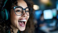 Young African American woman with curly hair wearing glasses and headphones laughing joyfully in office environment with blurred background. Positive workplace emotion.