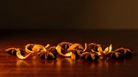 Dried star anise spices arranged in a row on warm wooden surface with dramatic lighting and shadows.