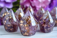 Amethyst crystal points with copper flakes in resin, handmade spiritual decorative objects on wooden surface with purple floral background.