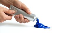 Hands squeezing blue acrylic paint from metal tube onto white surface for art projects and creative painting activities.