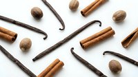 Aromatic baking spices scattered on white background featuring vanilla beans, cinnamon sticks and whole nutmeg for culinary and cooking projects.