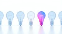 Glowing purple and pink light bulb standing out among transparent bulbs representing innovation, creativity and unique ideas in business concept.