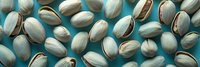 Roasted salted pistachios scattered on turquoise background, macro food photography showing texture and natural pattern of nuts in shells.