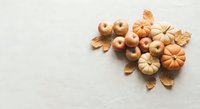 Autumn harvest composition with mini pumpkins, apples and dried leaves on neutral background for seasonal decorating and fall holiday designs.