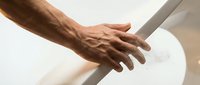 Close-up of mature male hand with visible veins and age spots gripping white handrail, depicting safety, support, and accessibility for elderly care or mobility assistance.