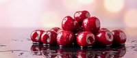Fresh red cranberries with water droplets on reflective surface against soft pink bokeh background for healthy eating and nutrition concepts.