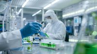 Scientist in protective suit conducting research with green liquid samples in modern laboratory facility for pharmaceutical development and chemical analysis.