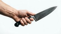 Male hand gripping a large sharp kitchen knife against a light background, conveying danger, crime, or culinary concepts.