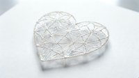Delicate white lace heart with intricate geometric pattern on soft fabric background for romantic wedding decoration and craft projects.