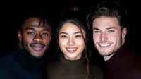 Portrait of three diverse young adults smiling at camera against dark background, representing friendship, teamwork and togetherness for lifestyle and social concepts.