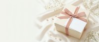 Elegant white gift box with pink ribbon bow surrounded by delicate flowers and pearls on soft beige background for special occasions and celebrations.