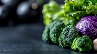 Fresh organic vegetables on dark background with copy space. Green broccoli florets, purple cabbage, and lettuce arranged in rustic composition.