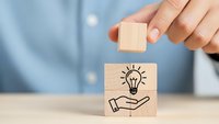 Businessman hand stacking wooden blocks with lightbulb and hand icons representing innovation, creative thinking and business solution concepts.