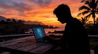 Remote worker typing on laptop at wooden desk during golden sunset with tropical ocean view and palm trees, freelance professional working outdoors.