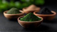 Vibrant green spirulina powder in wooden bowl with assorted superfood powders on dark background. Natural organic supplements for healthy nutrition.