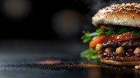 Fresh juicy beef burger with sesame bun, tomatoes, lettuce and sauce on dark background with copy space. Close-up of gourmet hamburger with selective focus.