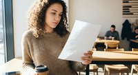 Young mixed-race businesswoman reading document in modern office cafe with coffee cup, professional workplace environment for corporate communication.