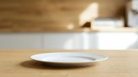 Empty white plate on wooden table with blurred kitchen background, suitable for food styling, restaurant menus, and culinary design projects.