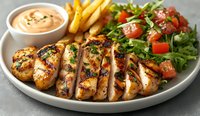Grilled chicken breast sliced on white plate with french fries, fresh garden salad and creamy sauce. Juicy meat with golden char marks served with sides.