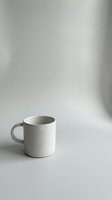 Minimalist white ceramic coffee mug on clean neutral background with soft natural lighting and shadows for modern kitchen and lifestyle concepts.