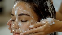 Young Asian woman receiving professional facial cleansing treatment at spa, white foam cleanser applied to glowing skin during luxurious skincare routine.