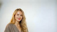 Young blonde Caucasian woman smiling warmly in casual gray top against clean white background for professional headshot and portrait photography.