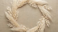Natural wheat ears arranged in circular wreath formation on beige linen texture background for harvest season decoration and rustic autumn design projects.