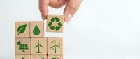 Hand placing wooden cube with recycling symbol among eco-friendly icons including solar panels, wind turbines and green leaves for sustainability concepts.