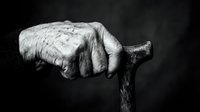 Elderly person's weathered hand gripping wooden walking stick against dark background, depicting aging, frailty, and dependence on mobility aids for daily life.