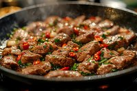 Juicy beef strips sizzling in cast iron pan with red chili peppers, fresh herbs and spices. Close up view of stir-fried meat with steam and cooking process.