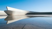 Futuristic white architectural structure reflected in still water under clear blue sky, suitable for modern design, corporate backgrounds, and contemporary art projects.