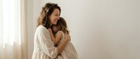 Smiling young Caucasian mother hugging her little daughter at home, sharing a tender moment of love and family bonding in a bright room.