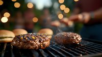 Juicy beef patties sizzling on barbecue grill with steam rising and bokeh lights in background, close-up view showing grilled meat texture and caramelization.