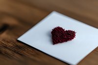 Red heart shape made from thread on white paper against wooden background, romantic minimalist composition for Valentine's Day or love message designs.