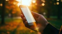 Hand holding smartphone with blank white screen outdoors in sunny autumn park, golden bokeh background, copy space for app or website mockup.