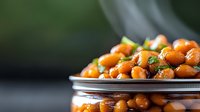 Fresh chickpeas garnished with herbs and spices on metal plate against dark background, selective focus on legumes creating appetizing healthy food composition.