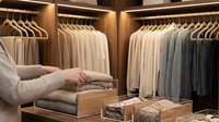 Person organizing luxury walk-in closet with wooden hangers and neutral clothing collection in modern wardrobe interior design.