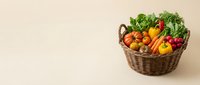 Fresh organic vegetables in a wicker basket on a beige background with copy space, showcasing a colorful harvest of tomatoes, peppers, and greens.