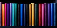 Colorful spines of books arranged in rainbow order on black background create vibrant library pattern. Multicolored hardcover volumes stand in neat row.
