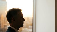 Professional businessman in suit silhouette looking through office window at sunset cityscape, contemplating future business opportunities and success.