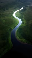 Aerial view of meandering river winding through lush green valley, creating natural curves and patterns in mountainous landscape. Dramatic lighting highlights water flow.